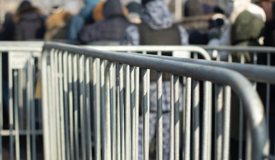 A close-up of extra steel fences used to keep lines orderly, with people in the background in a line for a concert.