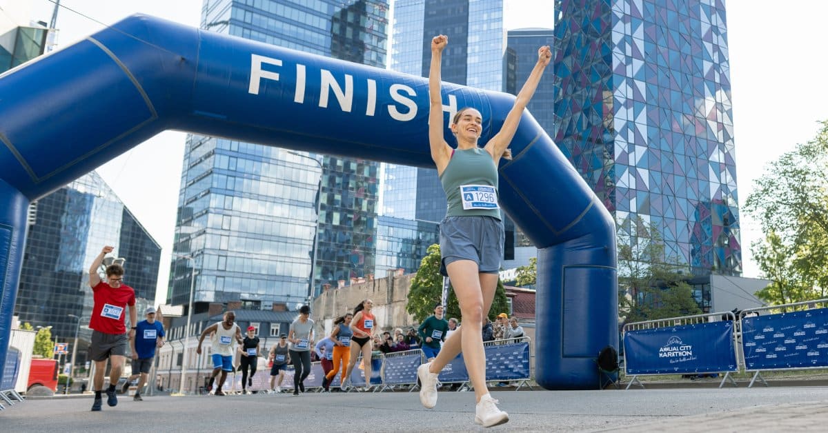 A woman cheering after she crosses the finish line of a race. Behind her, a large finish line inflatable stands.