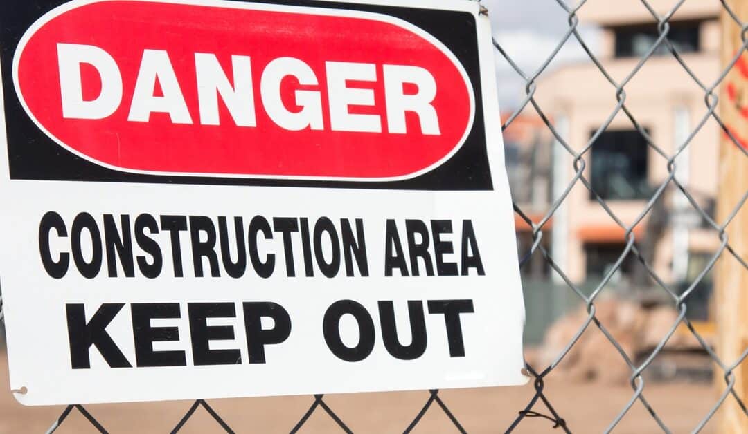 A chain link fence with a sign attached to it stating that this is a dangerous construction site and to keep out.
