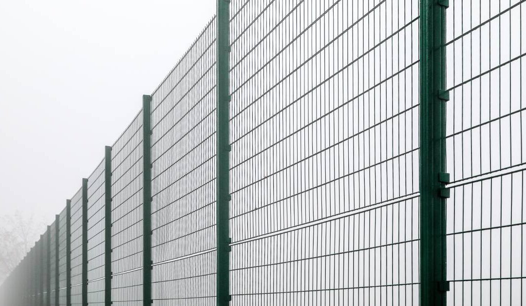 A tall and long fence that divides two spaces from each other. It is surrounded by fog and continues down the road.