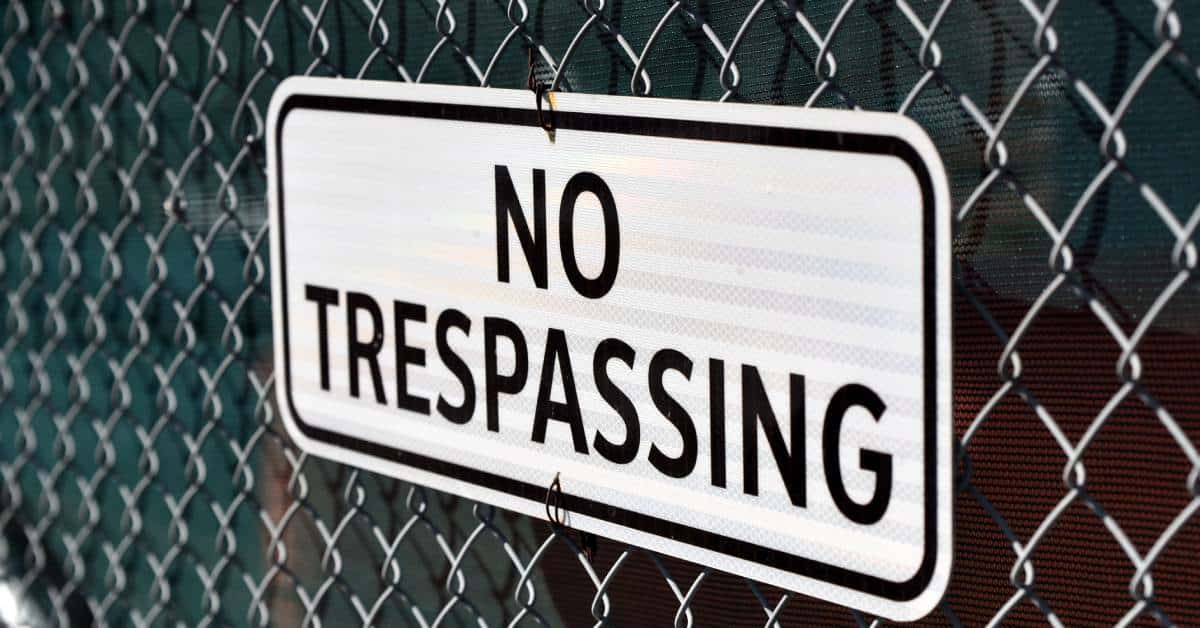 A chain link fence has privacy mesh attached to it. A sign that reads "NO TRESSPASSING" is on the fence.