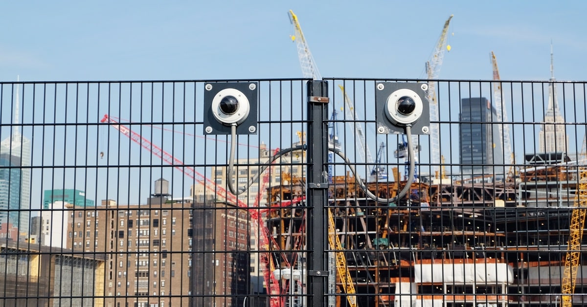 A construction site with black fencing around it. The fence also has security cameras attached to it to monitor.