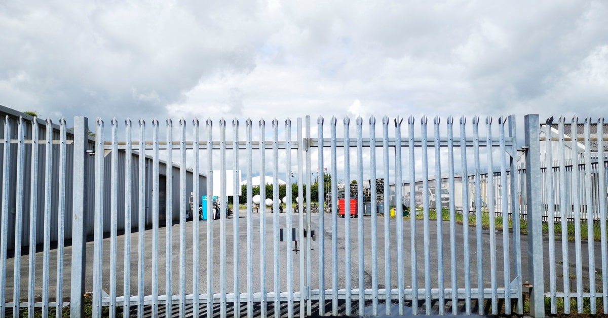 A light blue security fence blocking a parking lot. The fence is closed and located on a gray cement road.