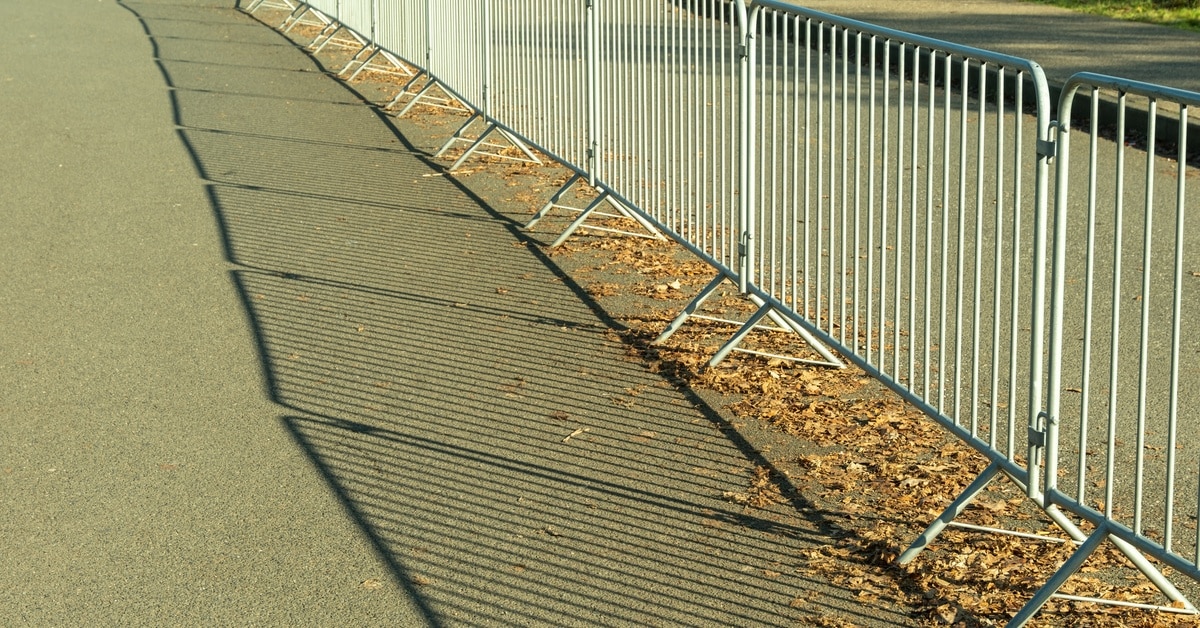 A long metal crowd control barrier lined up next to the road, preventing people from going past the asphalt.