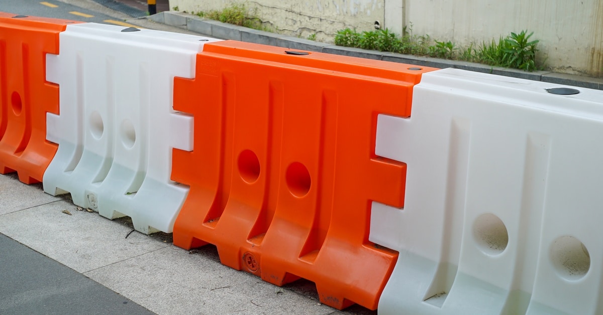 A traffic barricade with orange and white sections combined to form a longer chain. It is sitting next to a road.