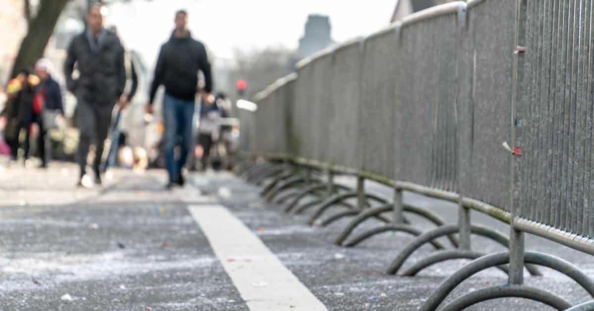 Metal fences linked across a road to allow people to walk without vehicle traffic. Two men are walking in the distance.