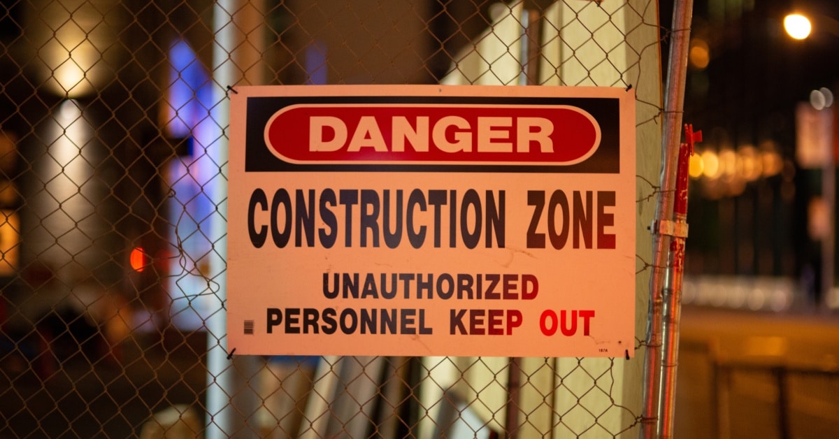 A construction site fence at night with a sign on it. The sign warns unauthorized personnel to stay out.