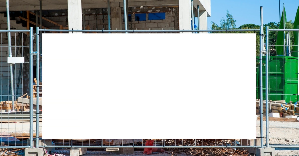 A temporary fence set up outside of a construction site with a white banner across the metal wiring.