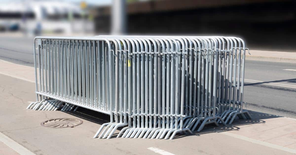 Multiple metal barricades stacked in line with each other. They are sitting in the middle of an empty road.