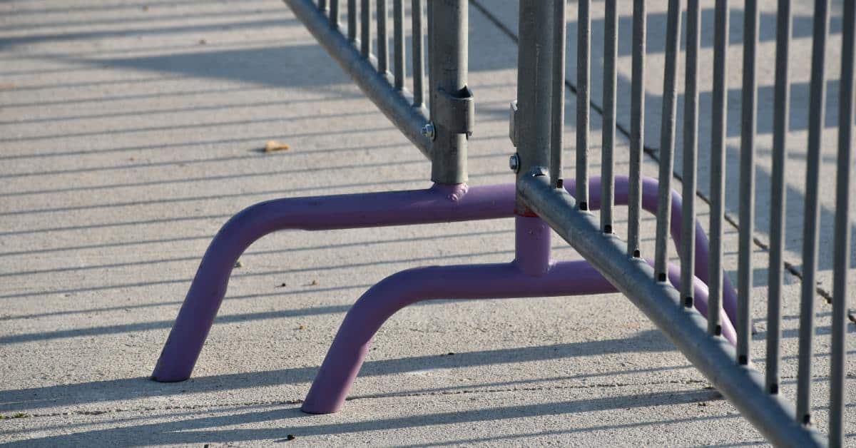 The bottom supports of temporary fencing set up for a local event. The fencing leaves shadows on the ground.
